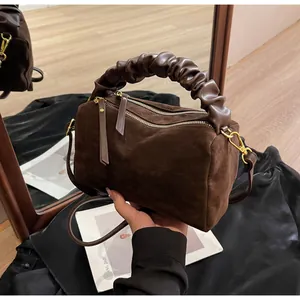 Λεπτομέρεια καφέ σουέτ τσάντας με σούρες στη λαβή και χρυσά μεταλλικά στοιχεία