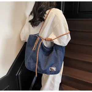 Detail of dark blue denim tote featuring braided orange rope strap and silver metal plaque