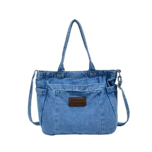 Blue washed denim tote bag with leather tag and adjustable shoulder strap on white background