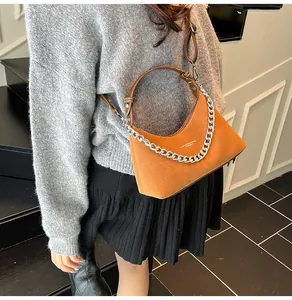 Dettaglio borsa a mezzaluna caramello con catena d'argento indossata da una modella