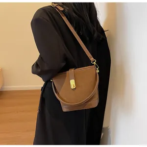 Détail d'un sac seau marron mat montrant le fermoir rotatif doré et la bandoulière en cuir