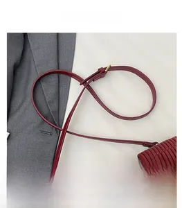 Detail of burgundy ruched handbag with adjustable leather strap and gold buckle