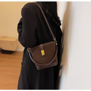 Model wearing a dark brown matte leather bucket bag with gold clasp and long shoulder strap