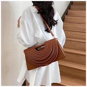Detail of caramel woven leather crossbody bag with pleated accordion layers on a staircase