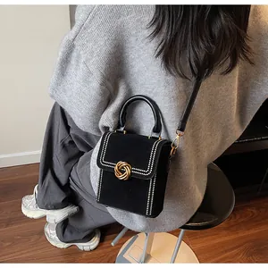 Λεπτομερής προβολή της μαύρης ματ τσάντας με χρυσό κούμπωμα κόμπο και διακοσμητικά καρφιά