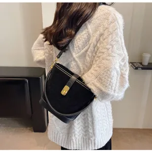 Détail du sac seau noir mat avec ferrures dorées porté sur l'épaule par le mannequin