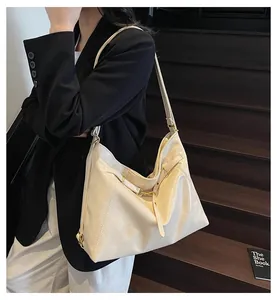 Off-white leather tote bag with shoulder strap worn by model on dark wooden stairs