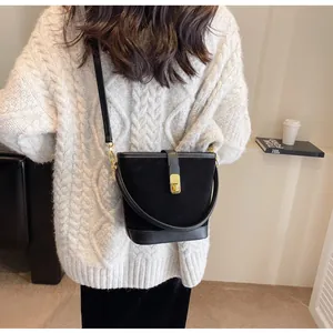 Détail du sac seau noir en daim mat avec fermoir doré porté par un mannequin