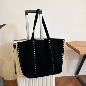 Λεπτομέρεια μαύρης σουέτ τσάντας tote με ασημένια τρουκς κρεμασμένη σε βαλίτσα