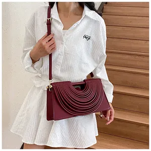 Detail of burgundy woven crossbody bag featuring layered crescent pleats and thin strap