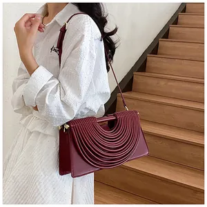 Detail of burgundy leather shoulder bag with embossed arch pattern on model