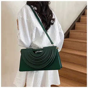 Detail of dark green woven handbag with arc pleats and gold hardware accents