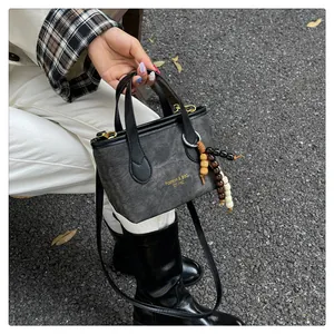 Detailed shot of dark grey denim bucket bag with beaded charm and gold hardware accents