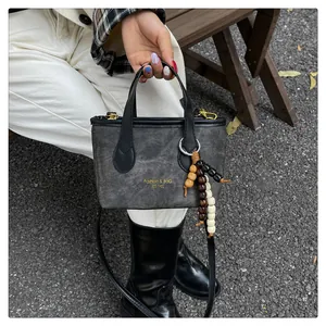 Close-up of retro gray canvas bucket bag with gold lettering and beaded charm detail