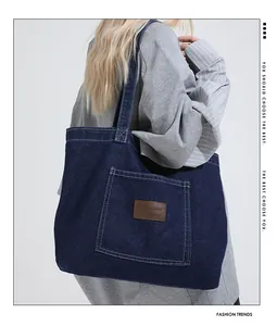 Detail view of a large dark blue denim tote bag featuring a leather logo patch on a pocket