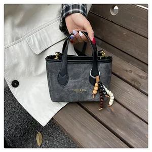 Close-up of gray canvas bucket bag with black leather handle and wooden bead charm