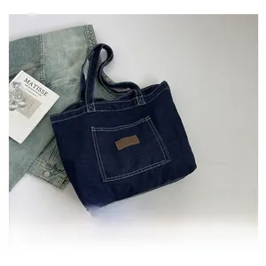 Detail of blue denim tote bag featuring front pocket and brown leather label patch