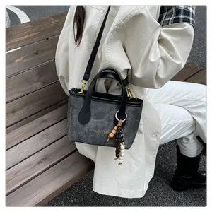 Detail of grey canvas bucket bag with black leather handle and wooden bead accessory