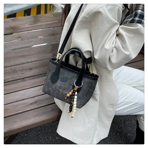 Detail of grey canvas crossbody bag with beaded charm and gold text on a wooden bench