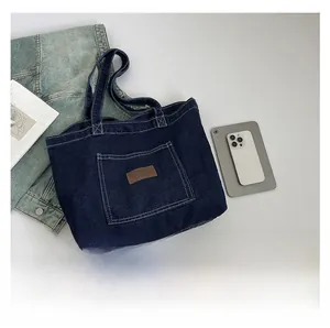 Detail of dark blue denim tote bag with leather patch, shown with magazines and tablet