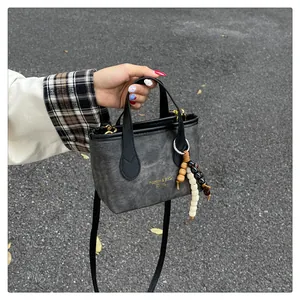 Detail of grey vintage bucket bag featuring gold logo text and colorful beaded charm