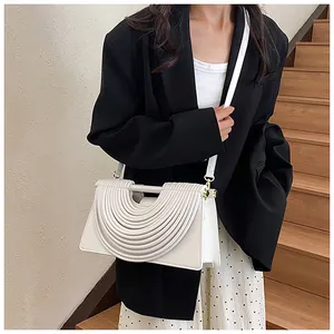 Detail of white pleated handbag with U-shaped design and gold hardware on a shoulder bag