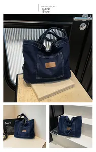 Detail of deep blue denim tote bag featuring dual handles and brown leather brand label