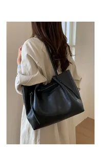 Detail of a large black leather tote bag with drawstring texture on a model shoulder