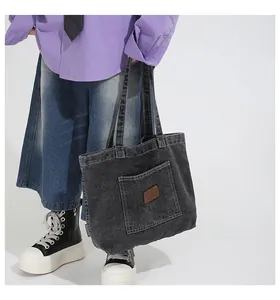 Detail of washed black denim tote bag featuring a front pocket and brown leather label
