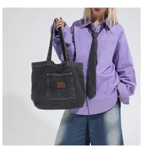 Detail of dark grey denim tote bag with visible stitching and a brown leather logo patch