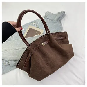 Λεπτομέρεια καφέ σουέτ τσάντας με χρυσή αγκράφα και πτυχώσεις στις δερμάτινες λαβές