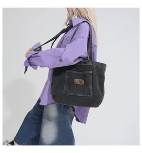 Detail of black vintage denim tote bag with a leather patch and external pocket on model