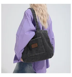 Detail of black denim tote bag showing exterior pocket and brown leather brand label