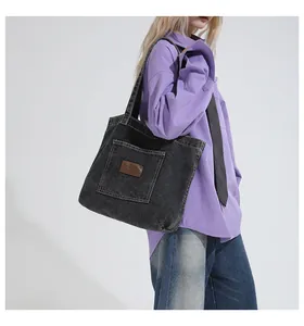 Detail view of a black denim tote bag with leather logo patch worn on shoulder