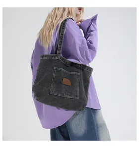 Detail of black denim tote bag with leather patch, shown on shoulder in a minimalist setting
