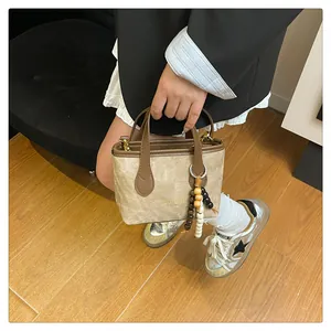 Detail of beige bucket bag featuring brown handles and colorful wooden bead charms