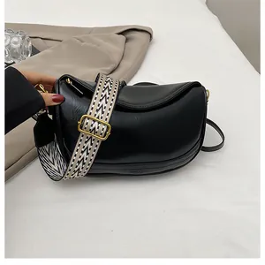 Detail of black leather half-moon bag featuring a wide geometric pattern shoulder strap