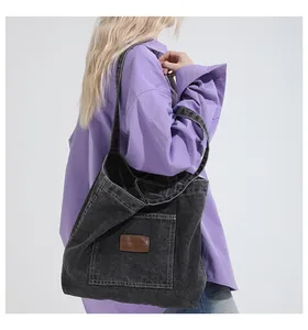 Close-up of black denim tote bag with front pocket and leather logo on purple shirt