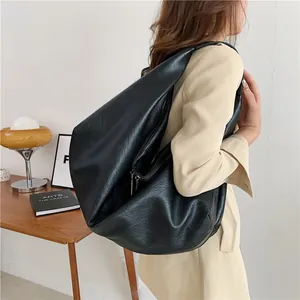 Large black slouchy tote bag in textured leather worn by model with beige blazer