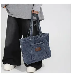 Detail of blue washed denim tote bag with side pocket and vintage brown leather patch