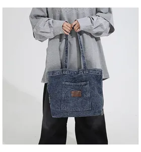 Detail of blue denim tote bag with front pocket and leather logo label on white background