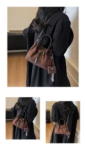 Detalle del bolso de cubo marrón mate con mini dije y correa ajustable para hombro
