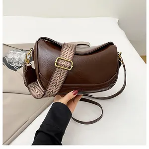 Detail of dark brown leather crescent bag with patterned wide woven strap and gold hardware