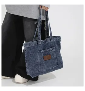 Detail of dark blue denim tote bag featuring a front pocket with a brown fashion label