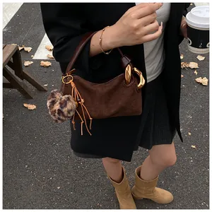 Close-up of vintage brown suede handbag with gold ring chain and leopard pompom detail
