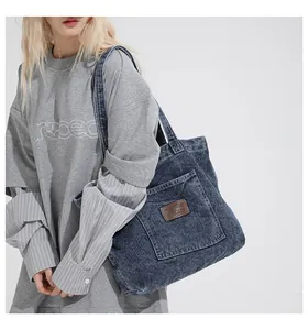 Detail of blue denim tote bag featuring a spacious front pocket and brown leather logo patch
