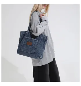 Detail of blue denim tote bag with brown leather patch and large front pocket