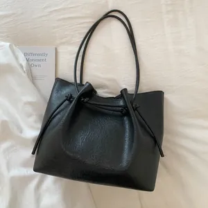 Detail view of black faux leather tote bag with drawstring knot on white fabric background