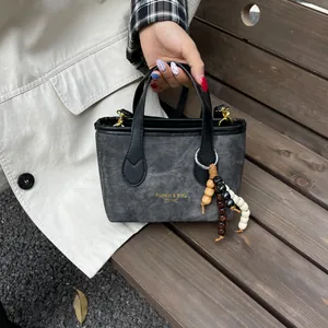 Retro grey denim bucket bag with leather handles and wooden bead charm on a wooden bench
