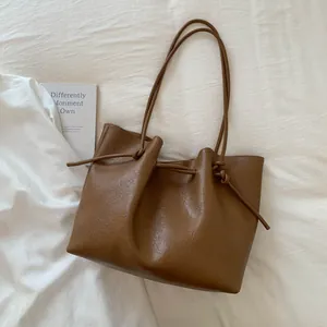 Detail of a brown textured PU leather tote bag featuring drawstring knot and slim straps